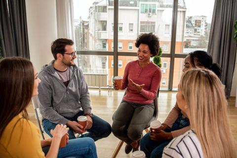 Diverse group of people sitting in circle drinking coffee.