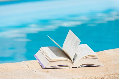 A hard cover book lies open on the edge of a swimming pool.