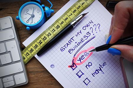 The words "start my own business? yes. no. maybe." written on a note pad. A hand holding a pen is checking the yes option.