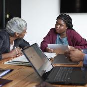 A young woman with a visual disability speaking with colleague at a conference room table.