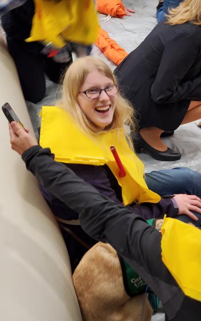 DSB Youth Services participant learns to use life vest and raft at an airline safety workshop hosted by Alaska Airlines. A flight attendant helps other participants.
