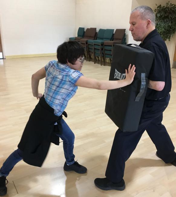 Student practicing self-defense by punching a large mat held by an instructor..